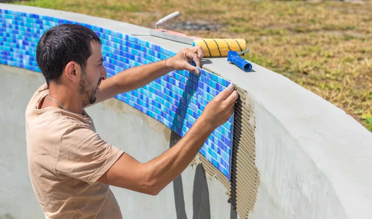 Worker laying mosaic tiles during a pool renovation